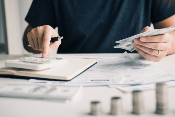 Man using a calculator and holding money to save for retirement in his other hand.
