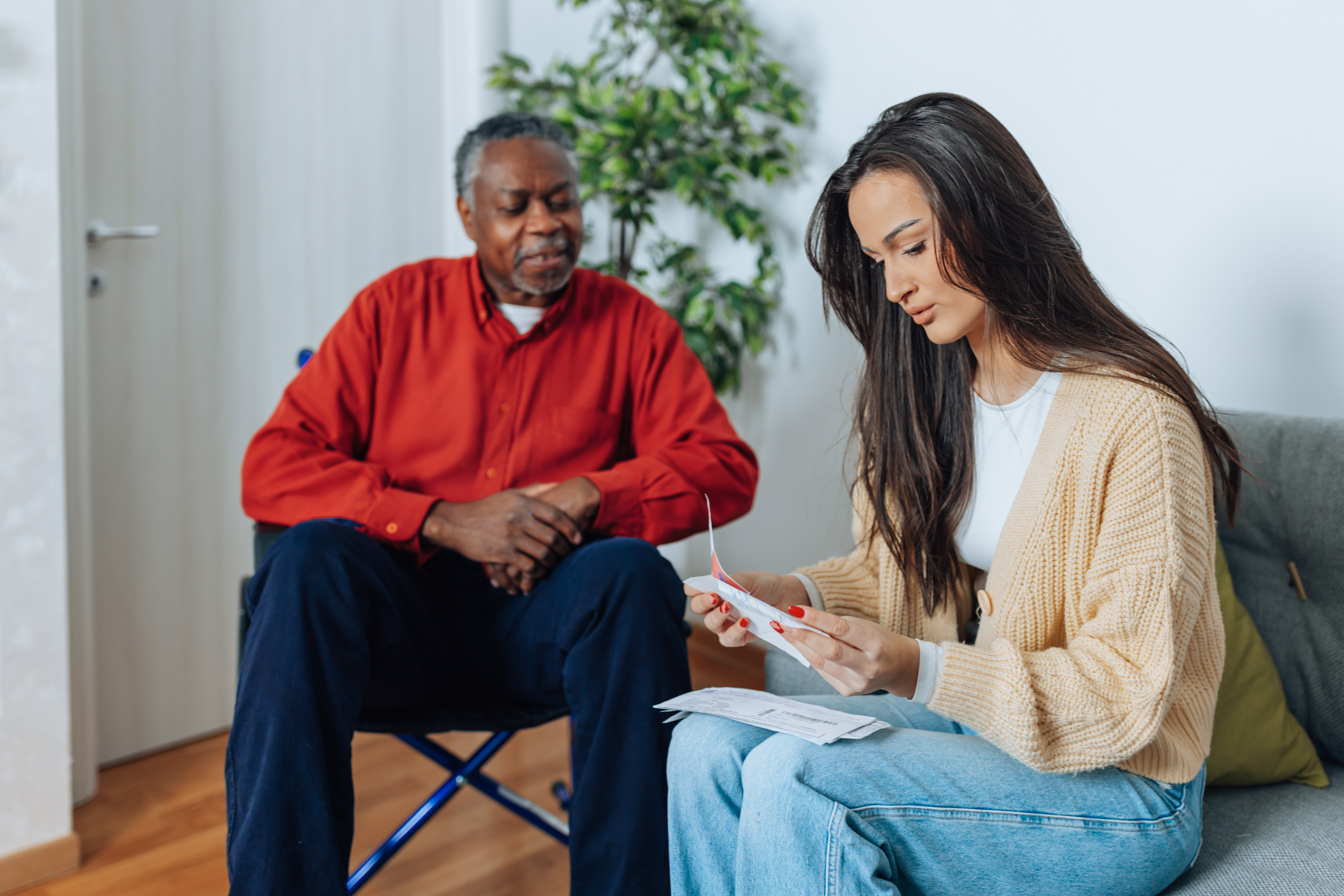 A young Caucasian female volunteer paying bills online to a senior African American man in wheelchair