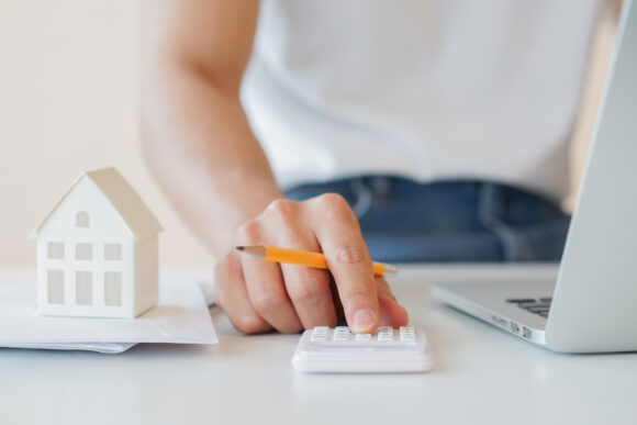 close up hand counting on calculator with house's model on invoice letter to summary of refinance expense for planning and manage money about home loan mortgage and interest rates for people lifestyle concept